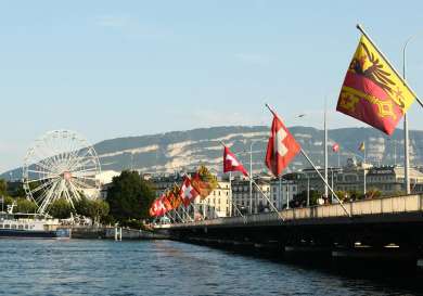 Pier with a ferris wheel and flags, with buildings in the background.