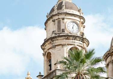 A clock tower with a palm tree in front of it.