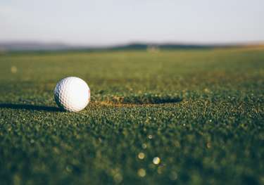 Golf ball sitting next to a hole on a golf couse.