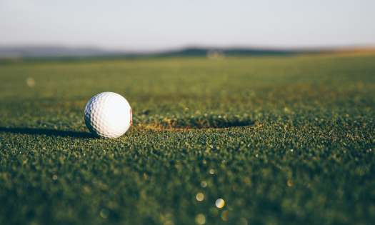 Golf ball sitting next to a hole on a golf couse.