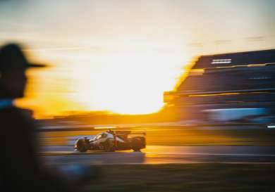 Blurry sunset behind a race car driving by on a track.