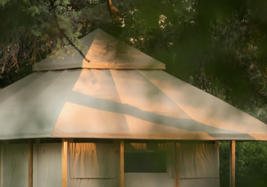 Large tan tent under leafy trees with filtered sunlight.