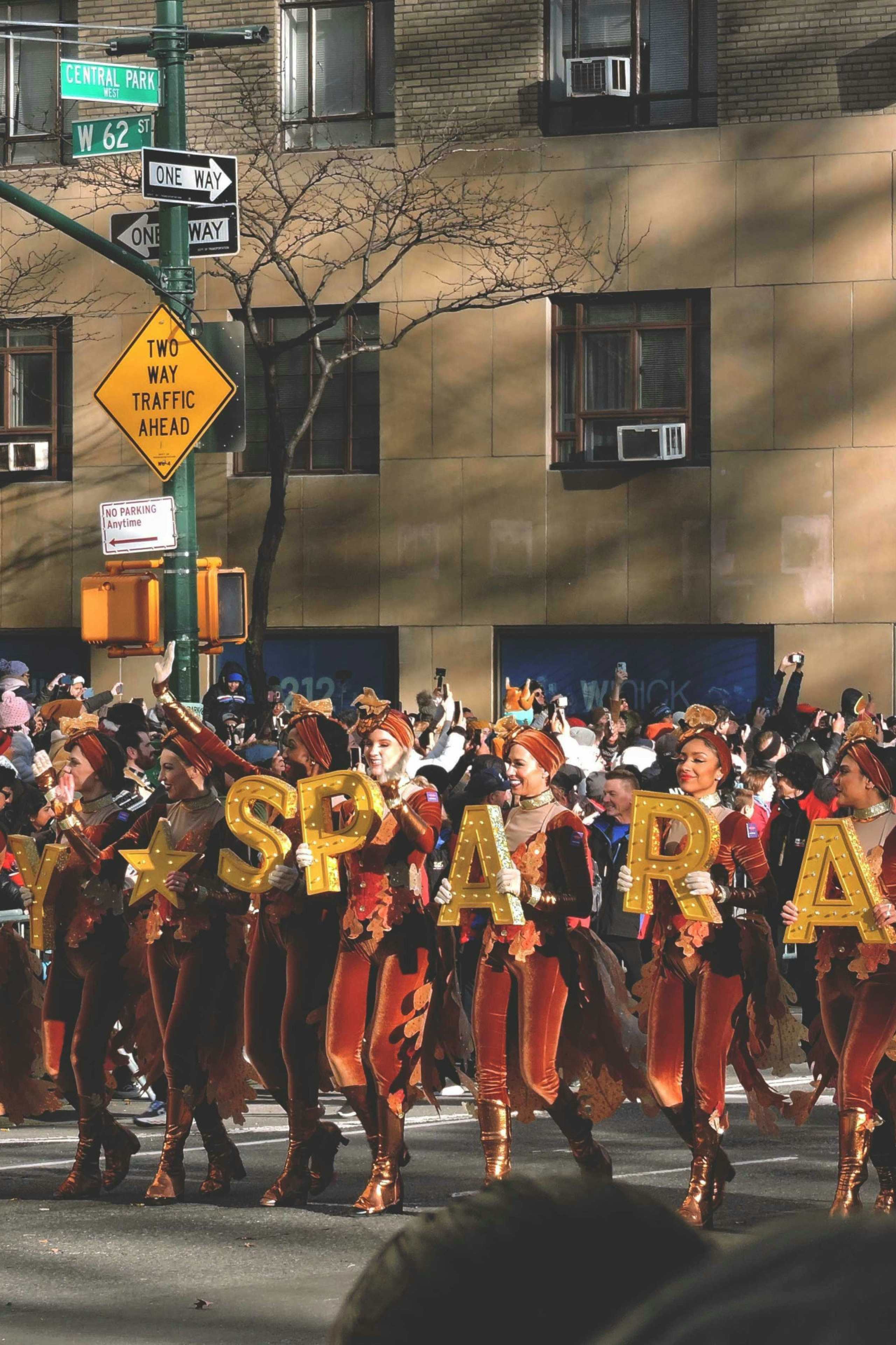people in a line holding up yellow letter signs spelling out "Macy's Parade"
