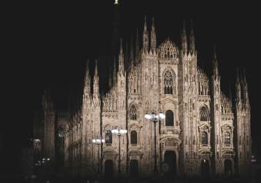 Duomo Catherdral in Milan at night with street lights in front.