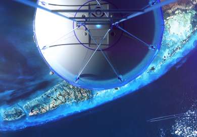 A large metallic sphere with geometric designs hovers above an oceanic scene, casting a shadow over turquoise waters and an island. The sphere is attached to several cables.