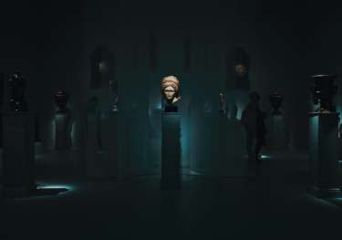 Dim-lit room with sculptures atop individual stands, one highlighted in the middle.