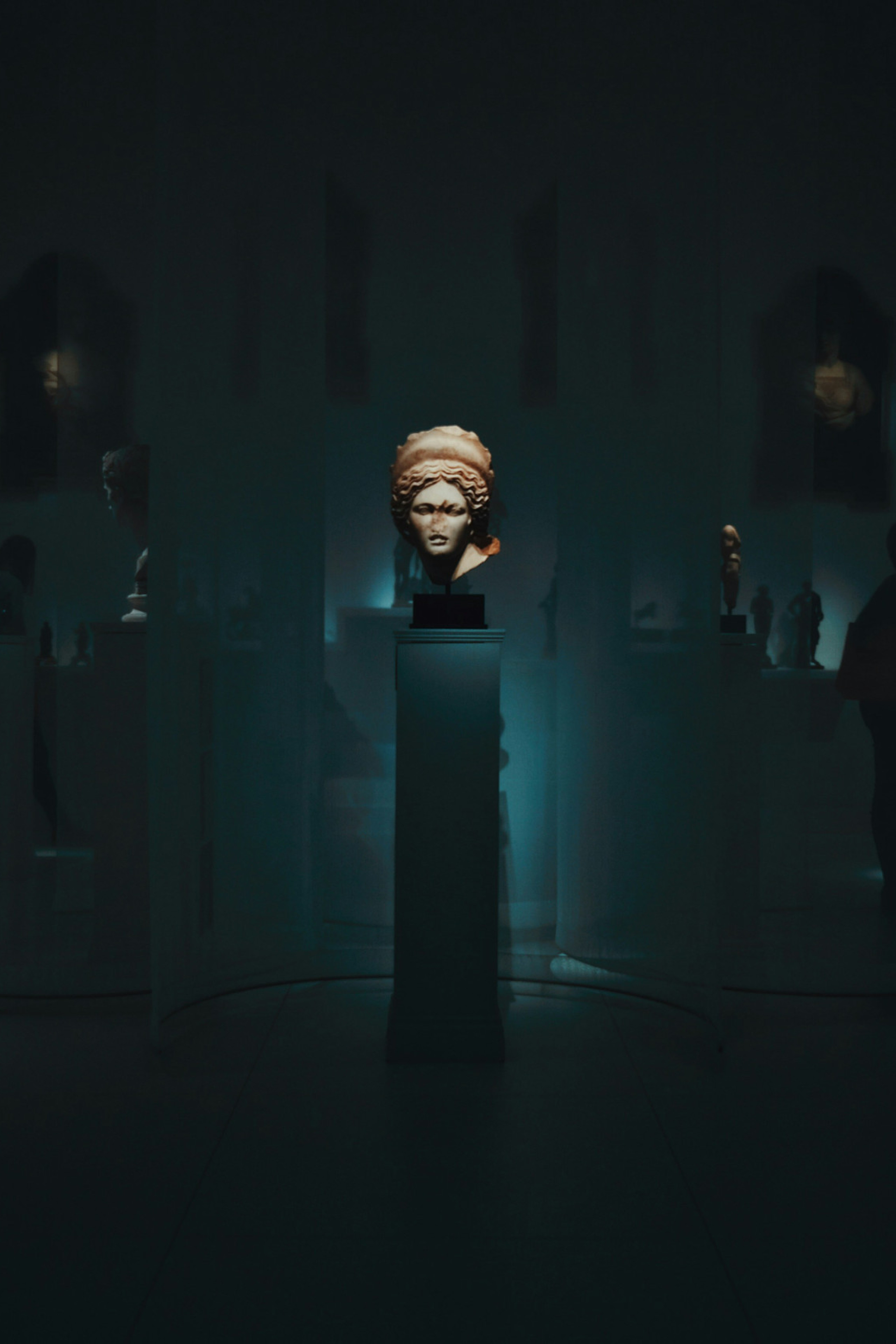 dim-lit room with sculptures atop individual stands, one highlighted in the middle