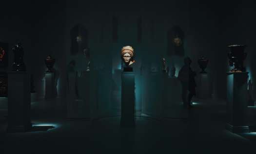 Dim-lit room with sculptures atop individual stands, one highlighted in the middle.
