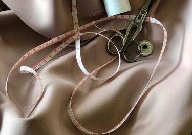 Silky fabric with measuring tape, scissors, and cotton thread.