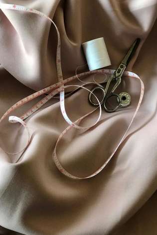 Silky fabric with measuring tape, scissors, and cotton thread.