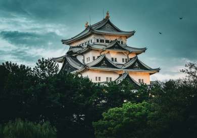 Nagoya Castle in Japan with a cloudy and dark background and green trees in front.