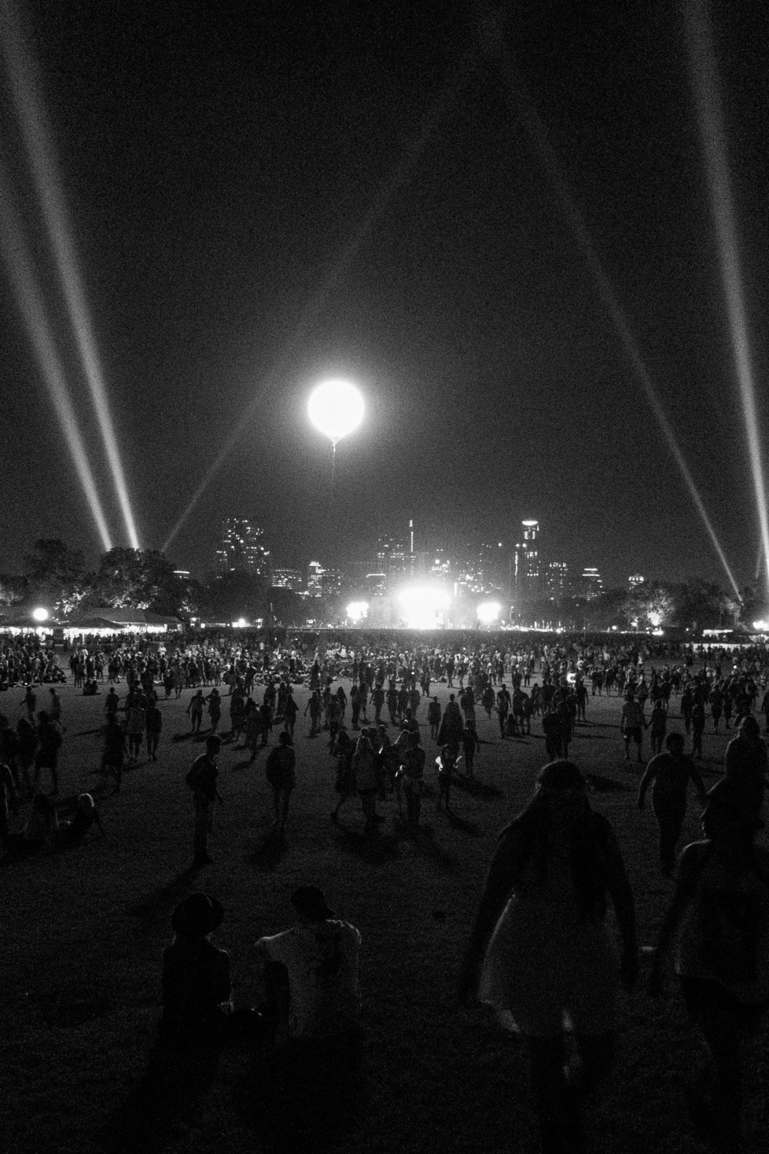 black and white image of a park at night with strobe lights and a bright moon above a stage