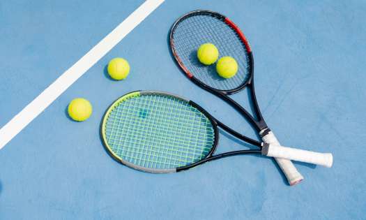 Two crossed tennis rackets on blue tennis court.