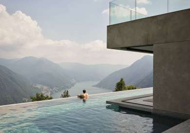 Man in an infinity pool overlooking a lake and mountains.