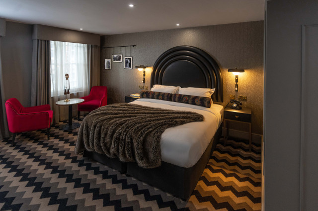 hotel gotham bedroom with zig-zag carpet and two red chairs