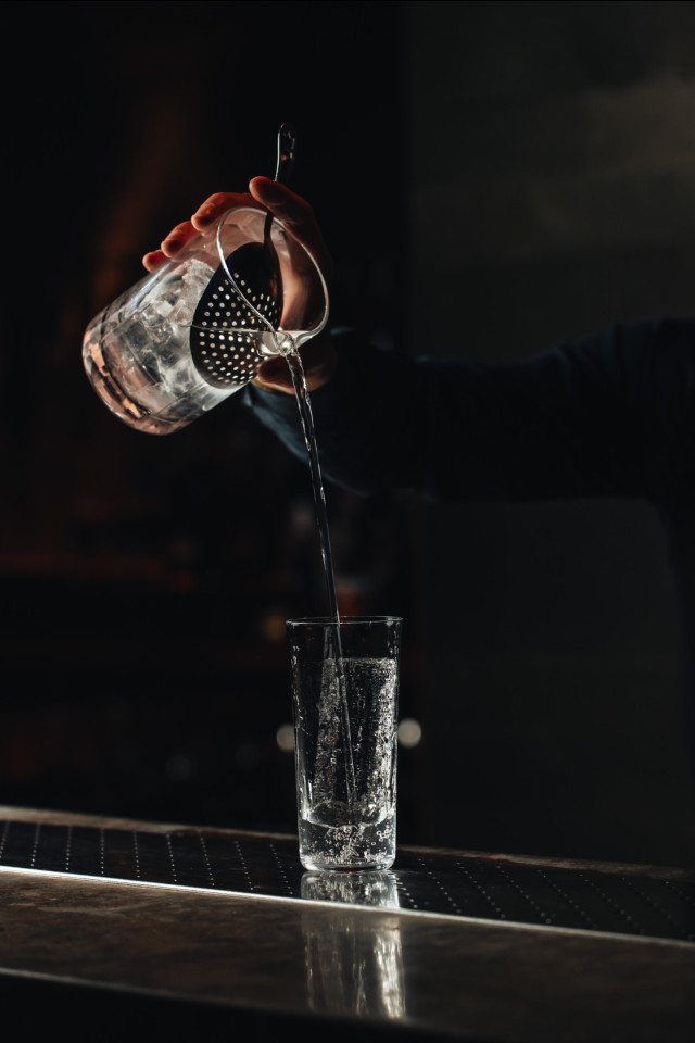 person pouring cocktail into tall glass