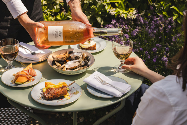person at table outside with glass of rose and lunch