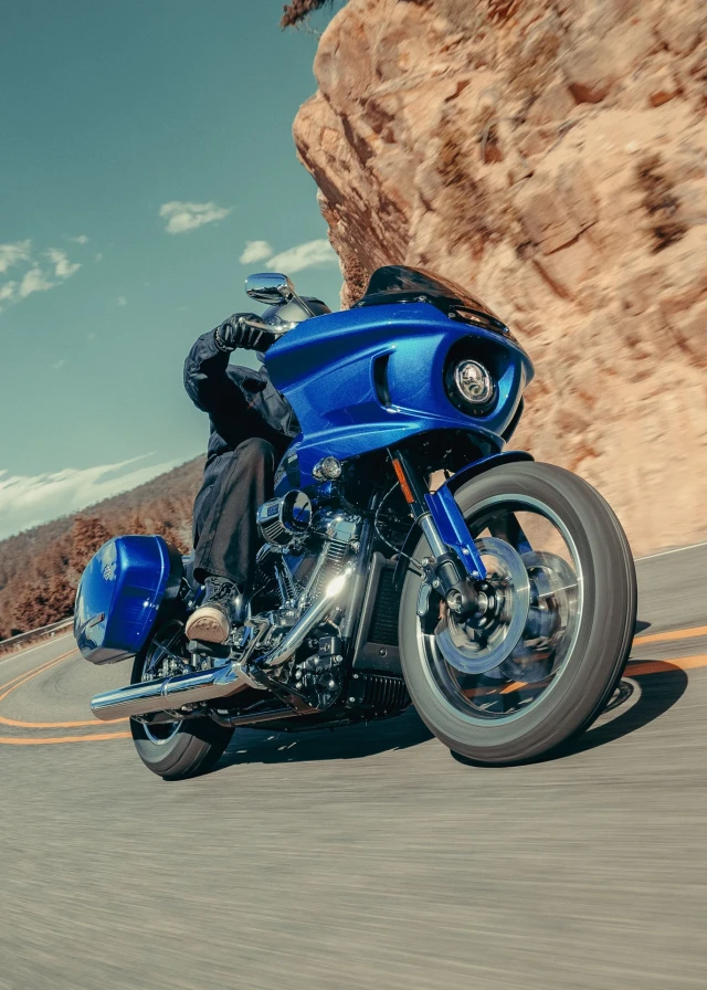 person riding harley davidson bike on road flanked by mountains