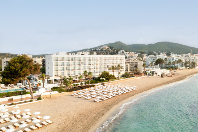 exterior of ibiza hotel next to the beach with mountains in the background 