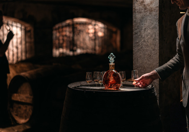 bottle of cognac placed on top of barrel with glasses 