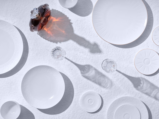 porcelain plates and bottle of cognac placed on white table 