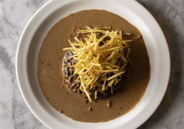 Meat dish with a sauce and thin potatoes .
