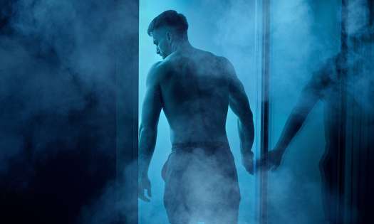 Man at sauna with blue lights shining through the door .