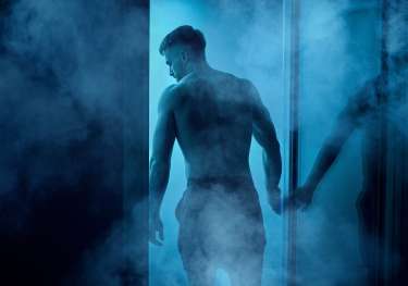 Man at sauna with blue lights shining through the door .