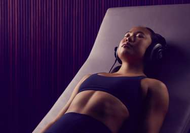 Gym user relaxing on lounger with headphones.