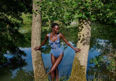 Model posing outside between two trees wearing sheer blue bodysuit .