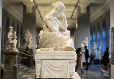 White statue of a woman sitting with her head resting on her hand.
