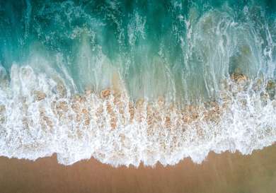 Aerial view of blue waves on golden sand .
