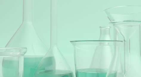 Scientific beakers on mint-green background.