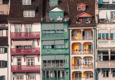 Colorful, multi-story buildings stand closely together, featuring red, green, and yellow facades with balconies.