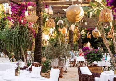 View of hotel restaurant with wicker chaires and hanging rattan lights.
