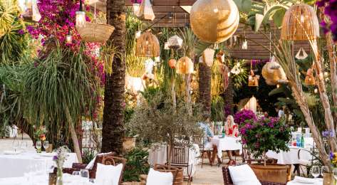 View of hotel restaurant with wicker chaires and hanging rattan lights.