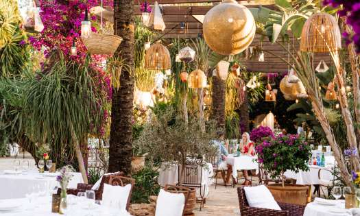 View of hotel restaurant with wicker chaires and hanging rattan lights.