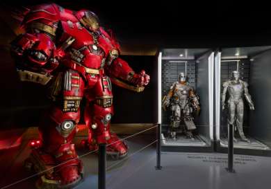 A large red armored figure stands poised, flanked by two smaller, display-cased silver armors.