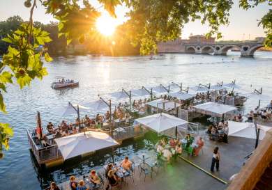 People sat eating outdoors on restaurant terrace in toulouse with the sun setting behind them.