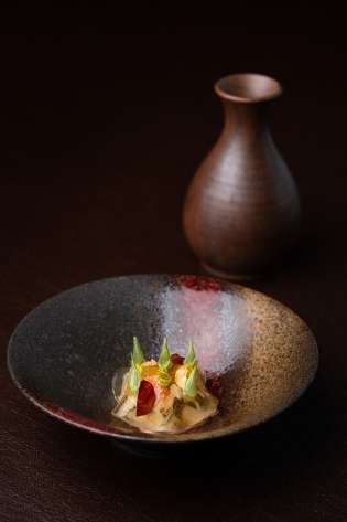 Crab salad dish on wooden table with small ceramic vase in the background.
