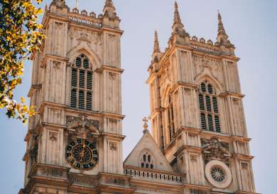 Towers with intricate Gothic architecture rise against a clear sky, framed by leaves.