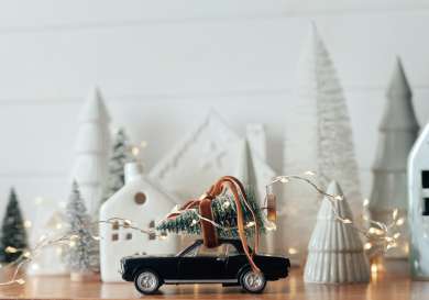 China display of white houses and toy black car with christmas tree on top.