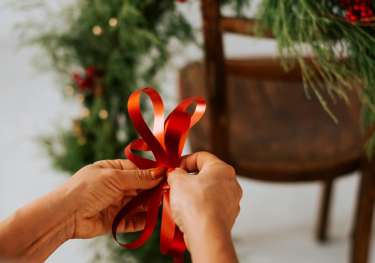 Person tying red ribbon with christmas wreath in the background.