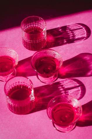Five glasses arranged on pink surface.