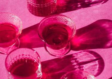 Five glasses arranged on pink surface.