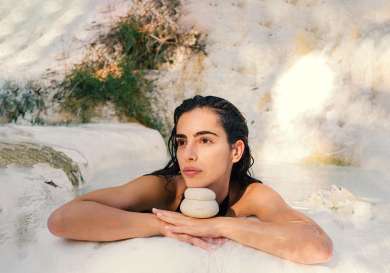 Woman in natural bath with chin on skincare product.