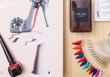 A book featuring a high-heeled shoe on a hand, paired with nail polish and color samples, sits on a wooden surface.