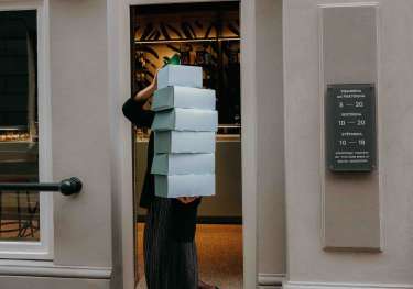 Person carrying blue boxes containing pastries.