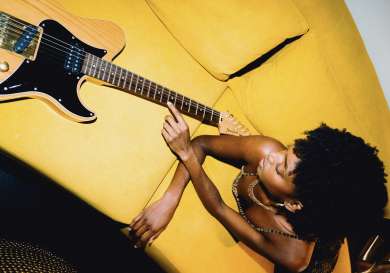 Woman lying on yellow sofa with wooden guitar.