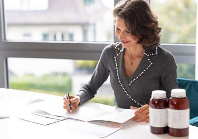Doctor writing notes in office with medication on the table next to her.